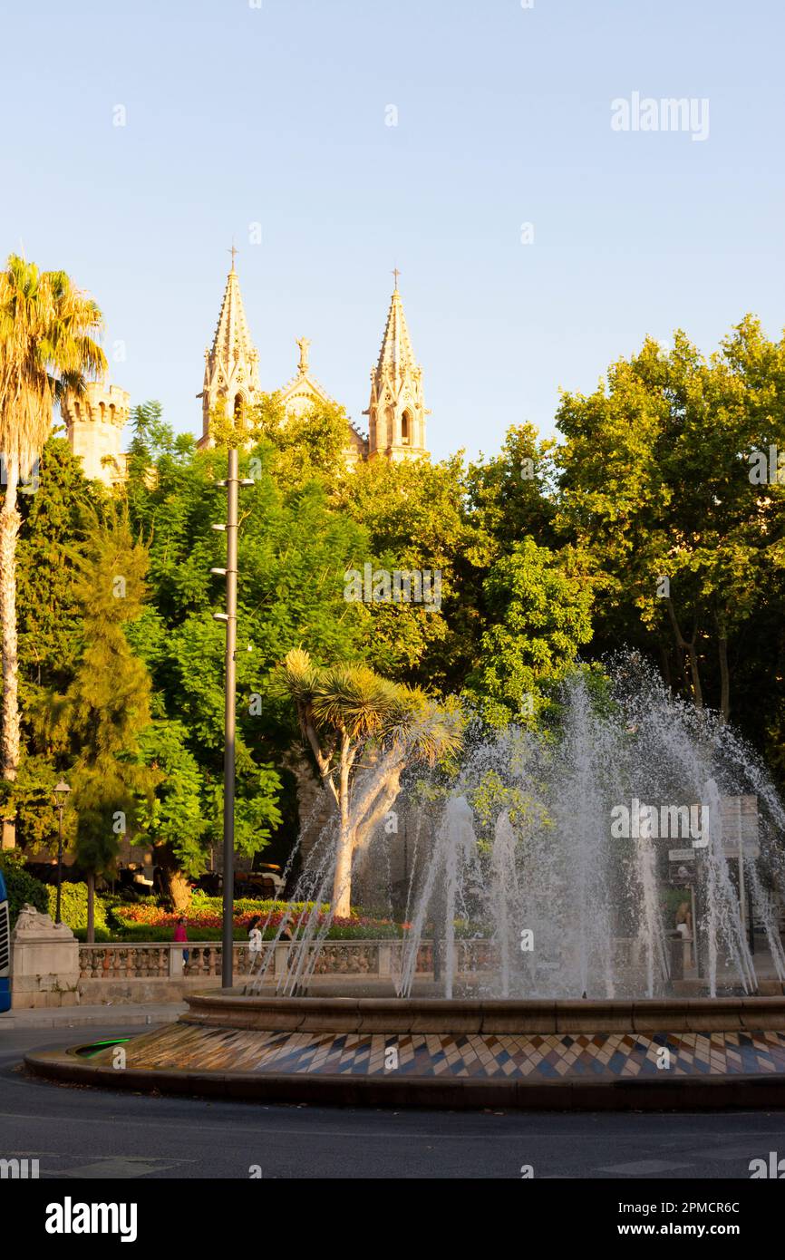 Palma, Mallorca, Balearic Islands, Spain. July 21, 2022 - Fountain in the roundabout of the Plaza de la Reina, or Queen square with the towers of the Stock Photo