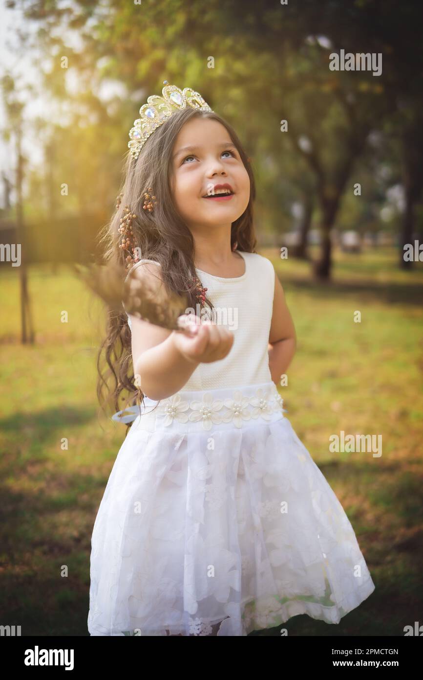 Little girl in white dress and princess crown, she poses for the camera with a beautiful look, copy space, children's day theme. Stock Photo