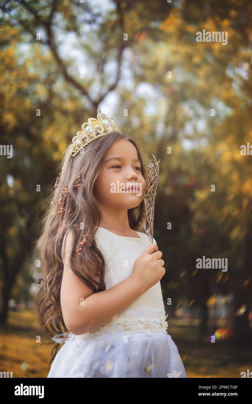 Girl in white dress and princess crown plays in the forest as in a fairy tale, copy space, children's day theme. Stock Photo