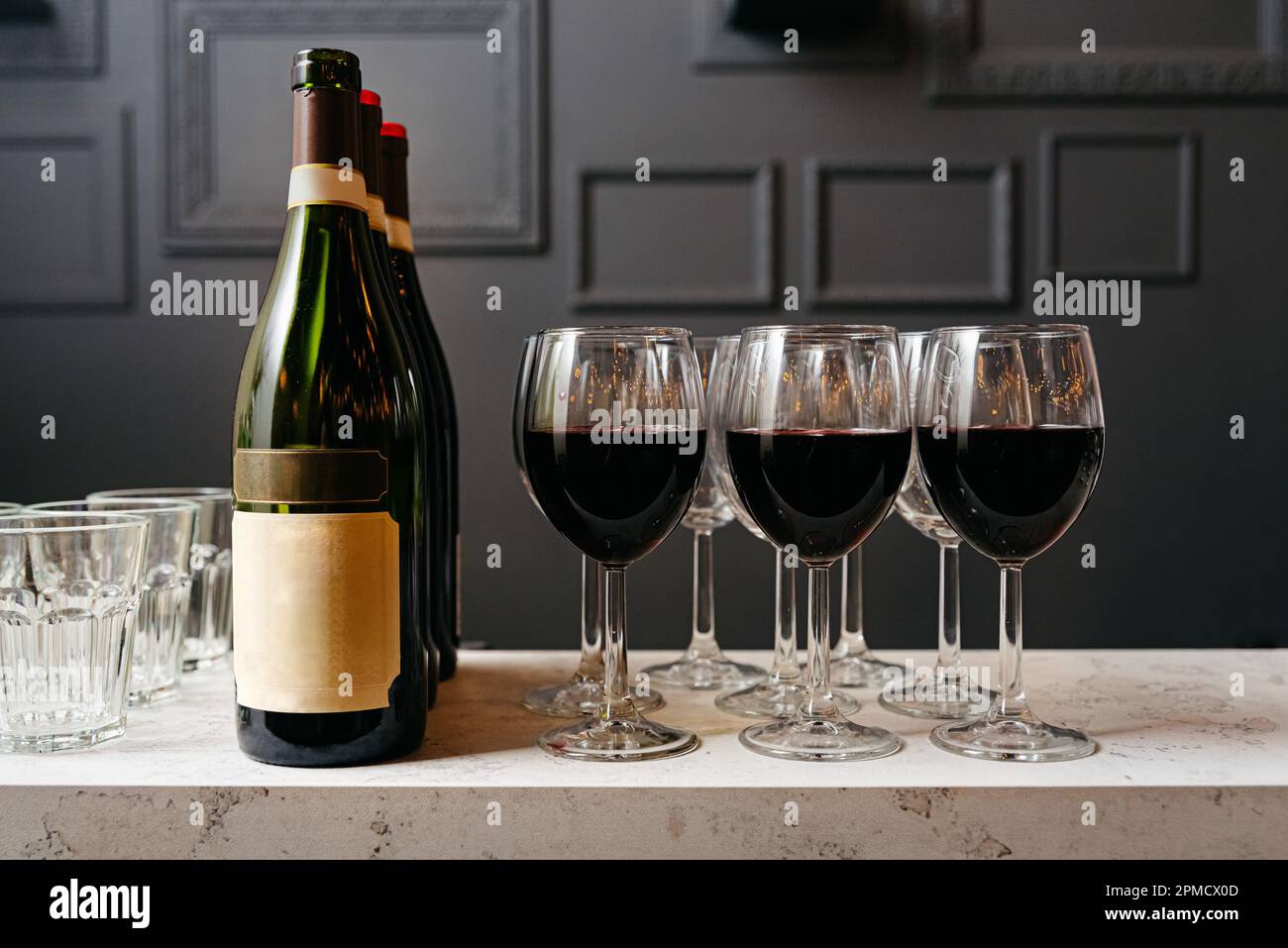 Bottle of red wine and glasses on the bar in the restaurant. Marble bar counter and black walls. Stock Photo