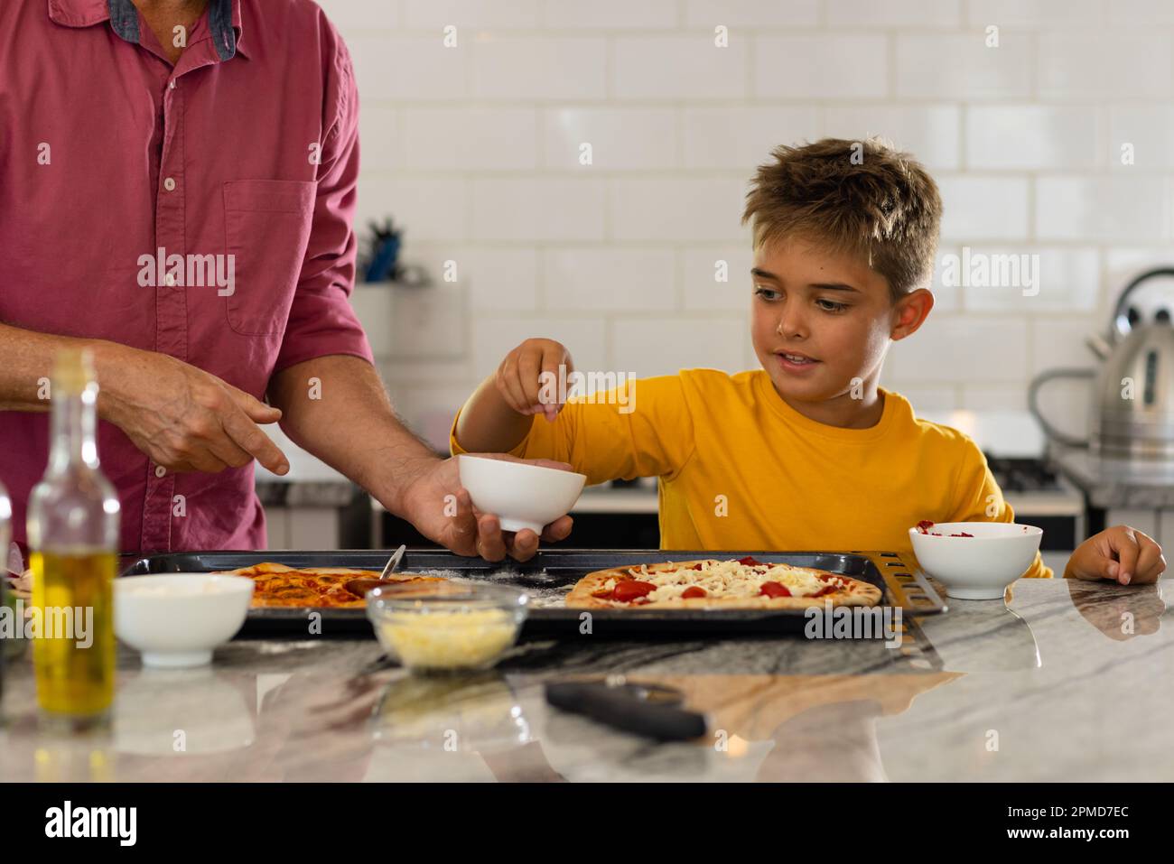 Midsection of caucasian senior man with cute grandson preparing pizza on kitchen island Stock Photo