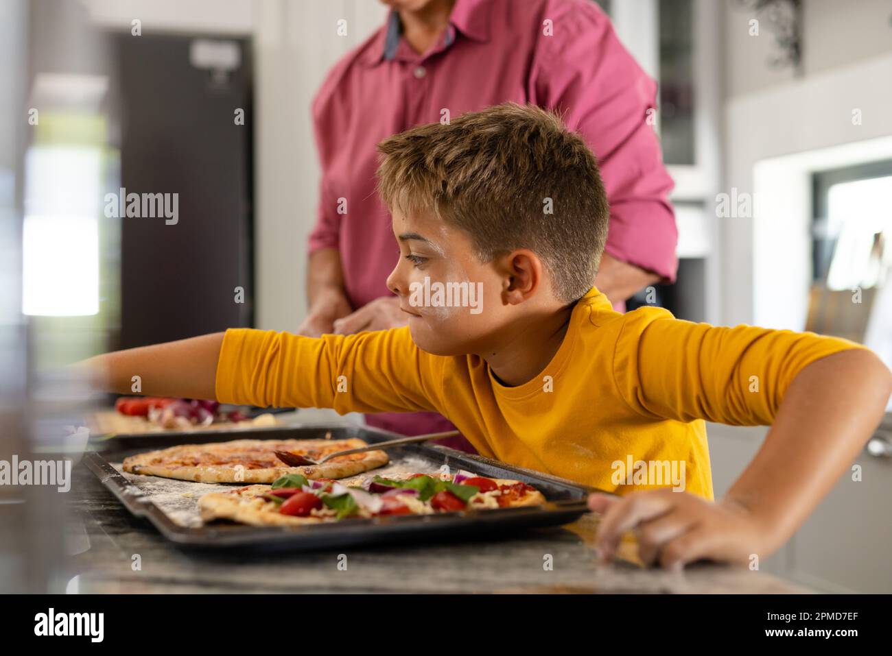 Midsection of caucasian senior man with cute grandson preparing pizza in tray on kitchen island Stock Photo