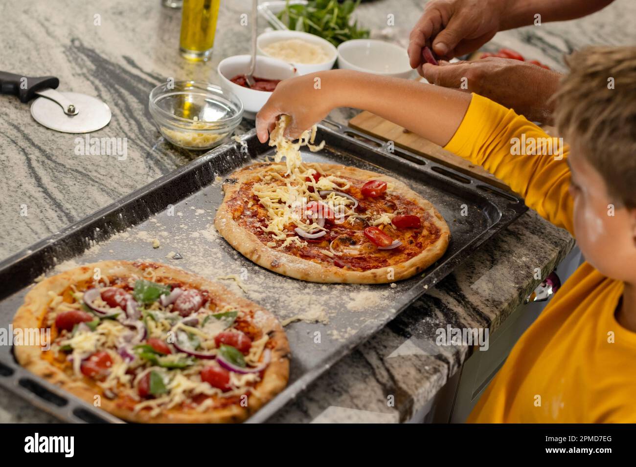 High angle view of caucasian boy arranging cheese on pizza in tray over kitchen island Stock Photo