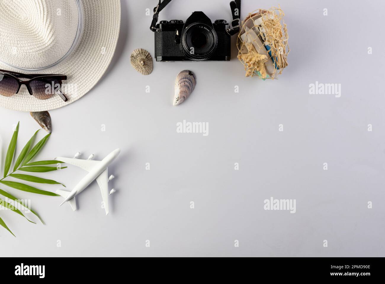 Airplane model, straw hat, sunglasses, camera and seashells on white