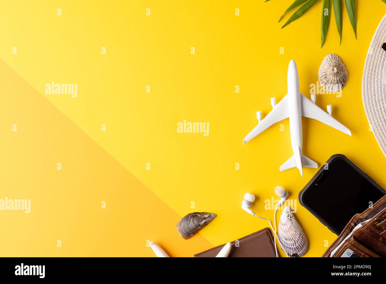 Airplane model, seashells, wallet, straw hat and smartphone on yellow