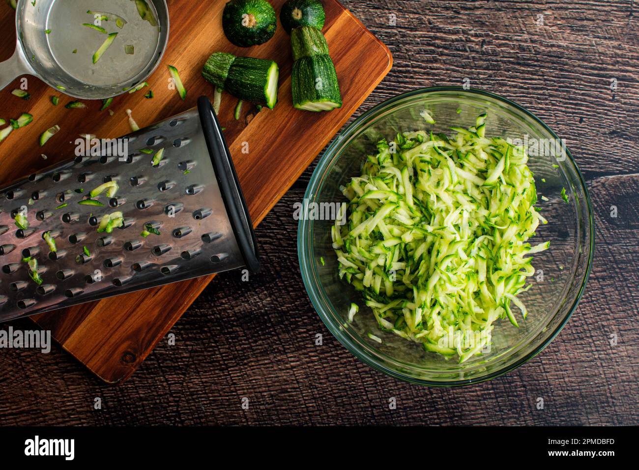 Shredded Zucchini in a Glass Mixing Bowl: Grated zucchini shown with a box grater and other tools Stock Photo