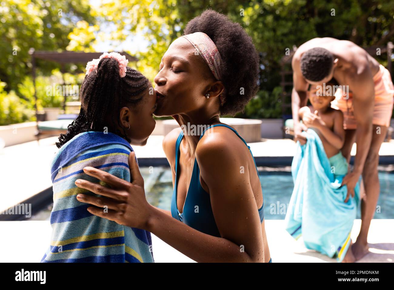 African american mother kissing on daughter's forehead and father wiping son at poolside in resort Stock Photo