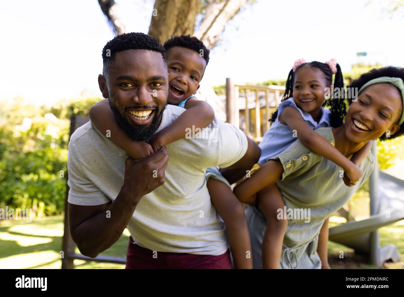 African american smiling parents piggybacking son and daughter while standing in playground Stock Photo