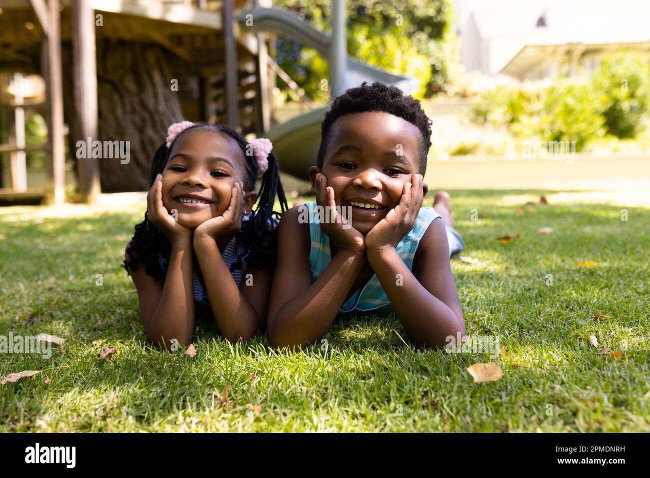 Portrait of cute african american siblings with hands on chins lying on grassy field in park Stock Photo