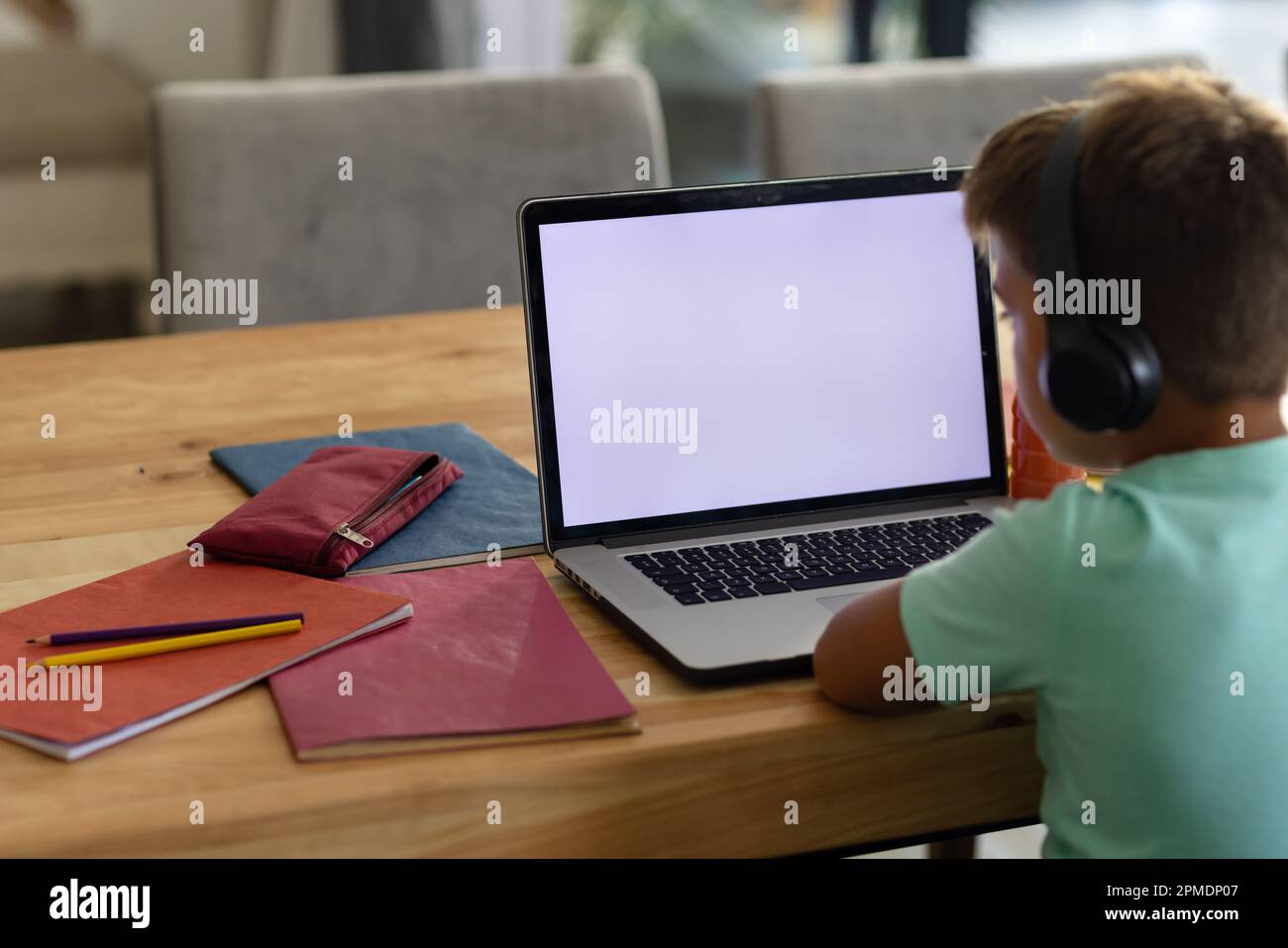 Rear view of caucasian boy with books on table wearing headphones and ...