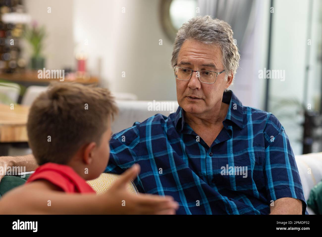 Caucasian grandfather looking at grandson shrugging shoulders while siting on sofa in living room Stock Photo