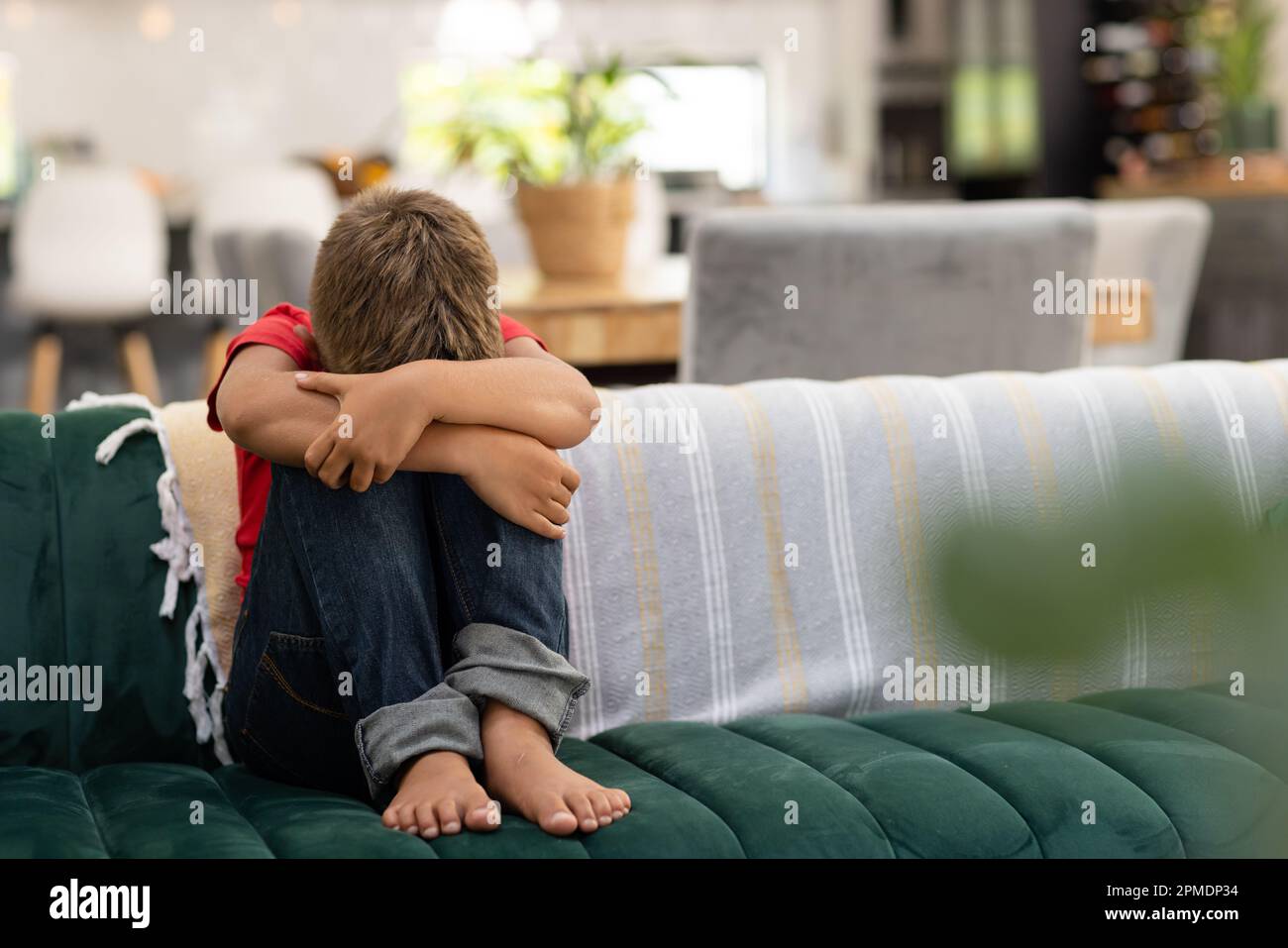 Full length of sad caucasian boy hugging knees while sitting on sofa in ...