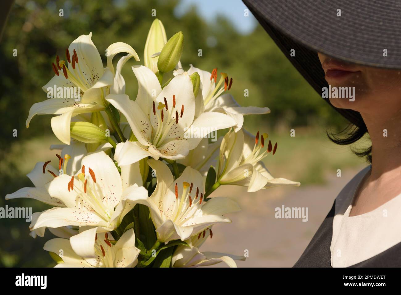 Bouquet of white lilies and a cropped portrait of a woman in a hat partially covering her face, side view. Stock Photo