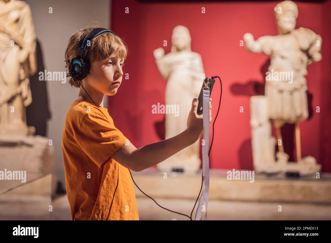 Boy looking at sculptures and listening to audio guide at museum ...