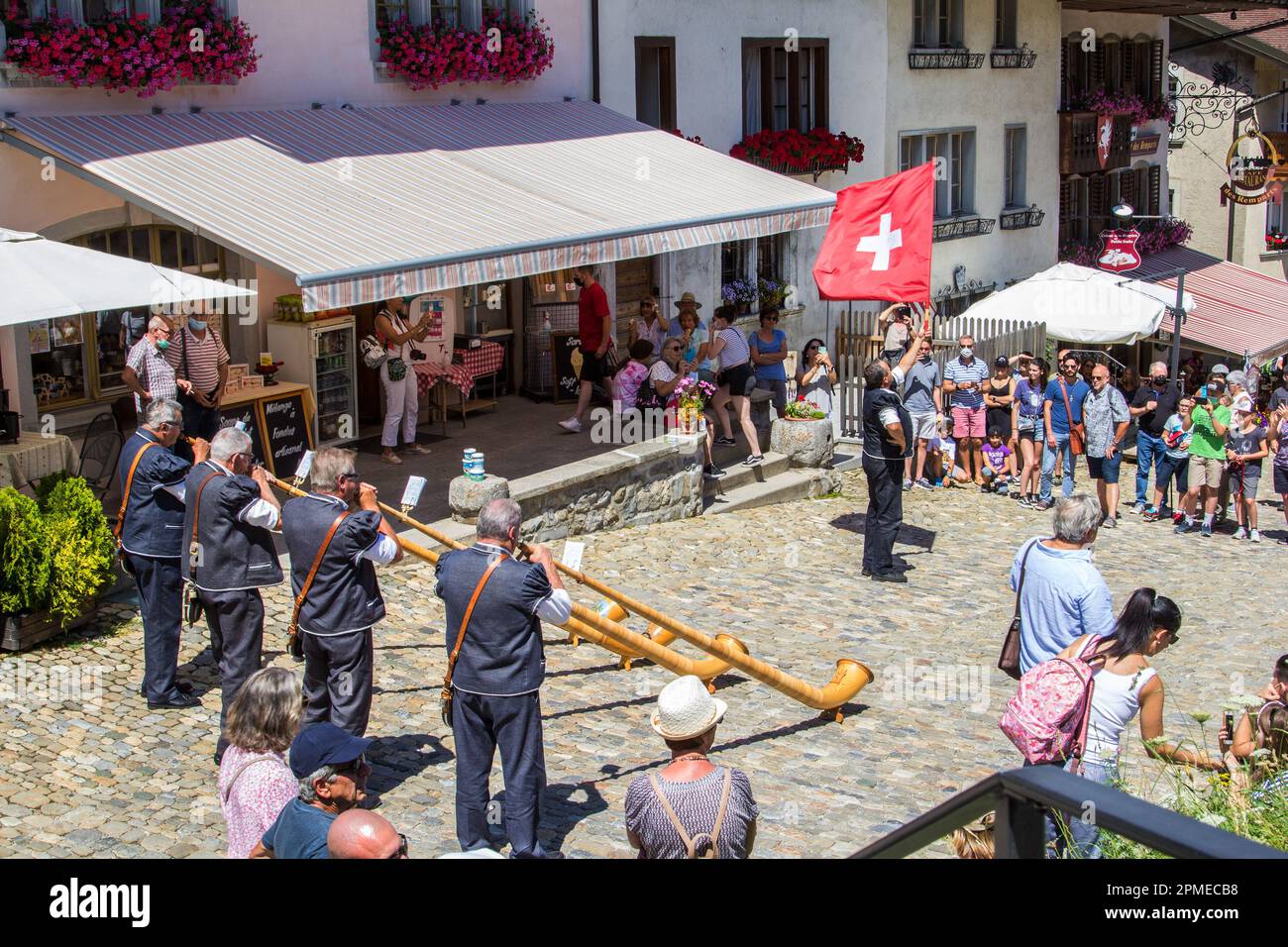 Gruyere, Switzerland - July 29.2021: A Swiss musician group play the traditioanl music instrument alphorn with a flag bearer to swing the National fla Stock Photo