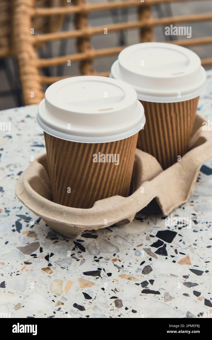Two paper cups with lid for tea to go. Coffee take away on the table.  Take-out coffees with brown paper cup holder. Brown safety cardboard  collars. Take away box for cups. Cardboard