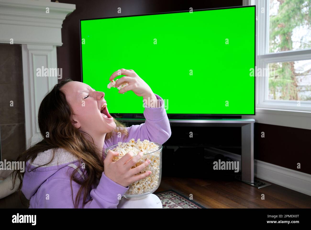 Shocked little teen children girl watching comedy video tv program or movie film content eating popcorn on comfortable sofa at home alone. Small cute school toddler Relaxation time. Stock Photo