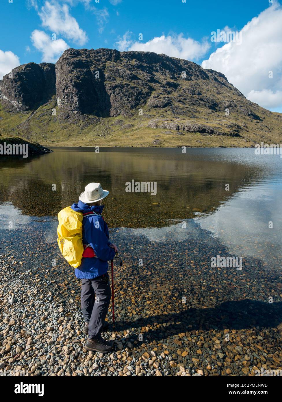 Female hiker with rucksack standing on the shore of Loch na Creitheach with the crags of Sgurr Hain in the Black Cuillins beyond, Camasunary, Skye, UK Stock Photo