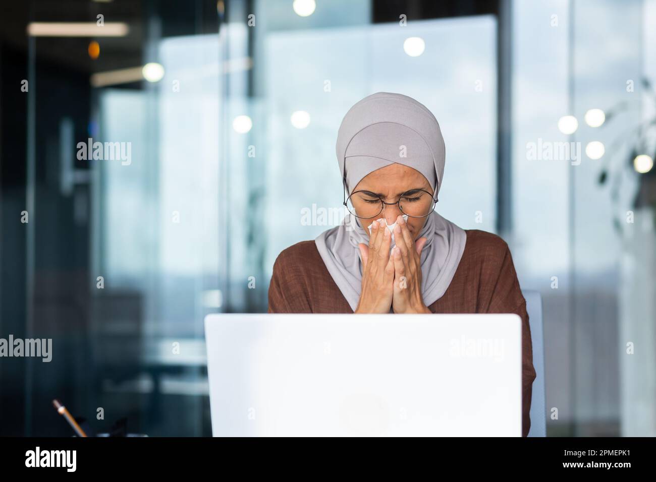 Businesswoman sick at workplace, Muslim woman in hijab sneezing and 