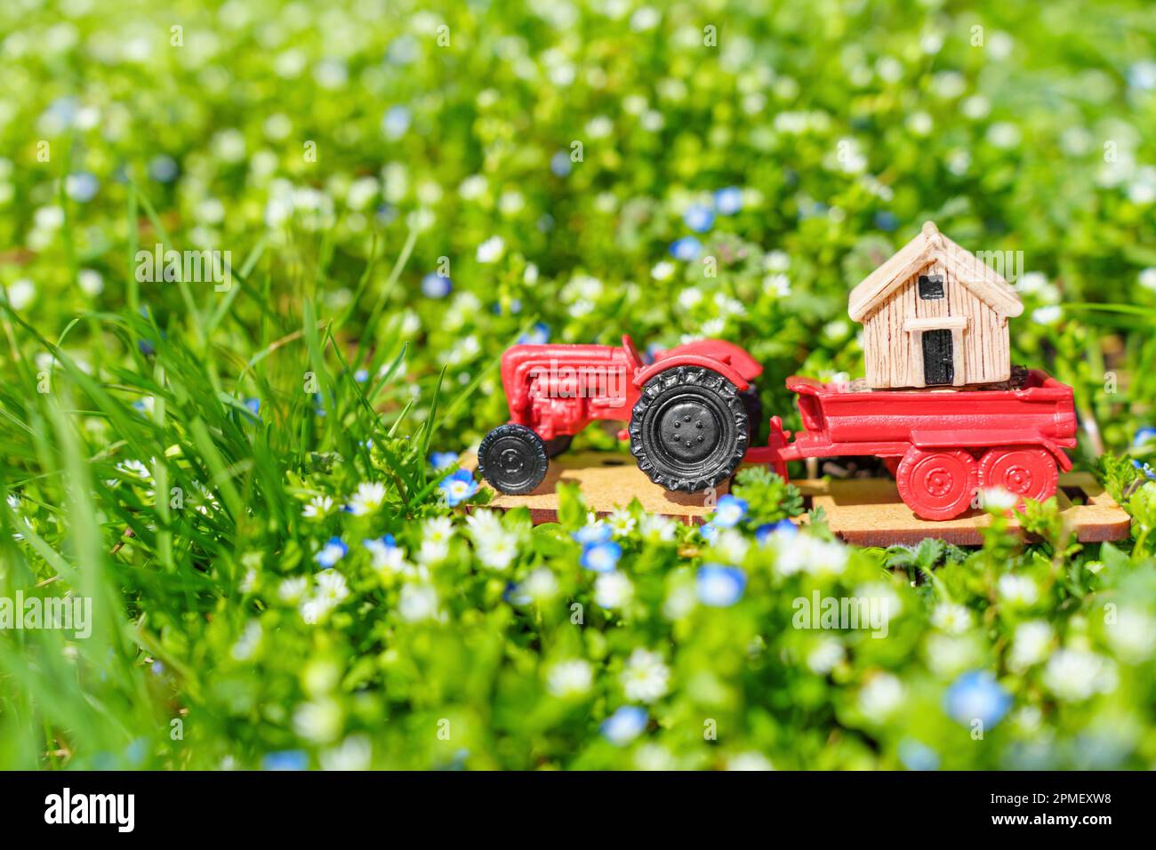 Miniature move: Toy tractor carrying a tiny house on a meadow of fresh ...
