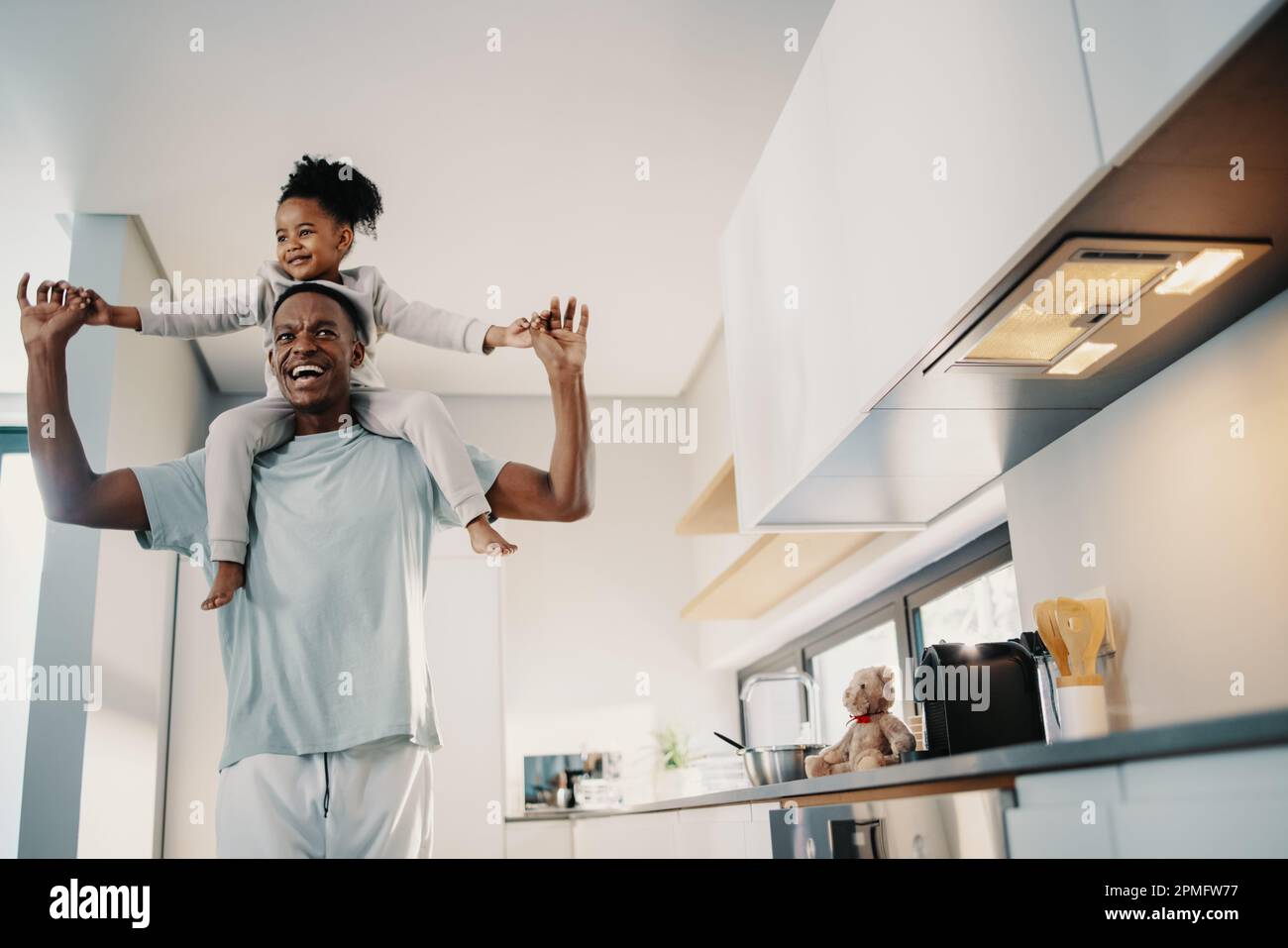 Father carrying his daughter on his shoulders, he smiles and holds her hands outstretched. Man playing with his daughter at home. Family fun between f Stock Photo