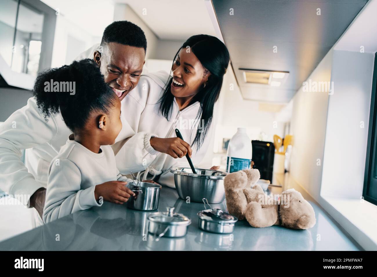 African family enjoying making breakfast together at home. Parents are talking and laughing with their daughter as they teach her how to prepare food. Stock Photo