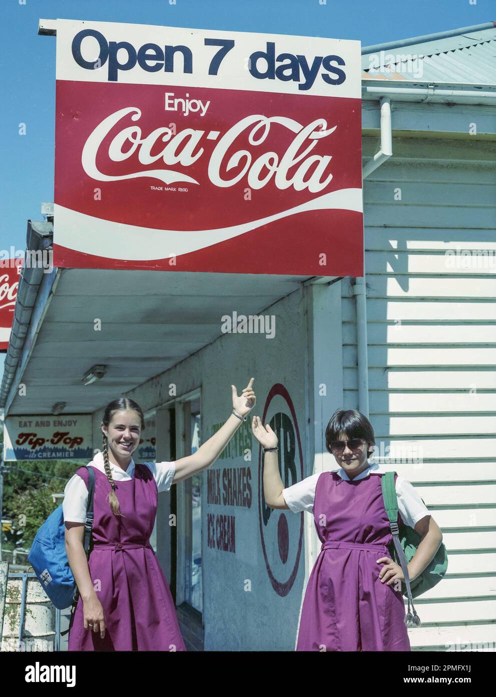 A 1981 historic image of teenage high school students pointing up to a Coca-Cola sign outside a Dairy store on the South Island of New Zealand Stock Photo