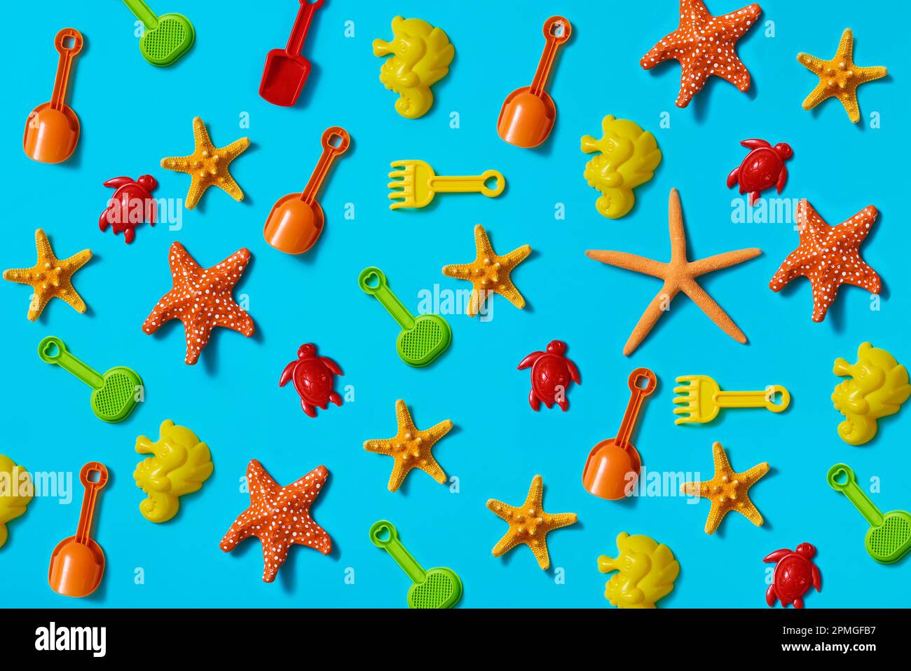 some beach shovels and rackets, some sand molds in the shape of seahorses and turtles, and some natural and fake starfish on a blue background Stock Photo