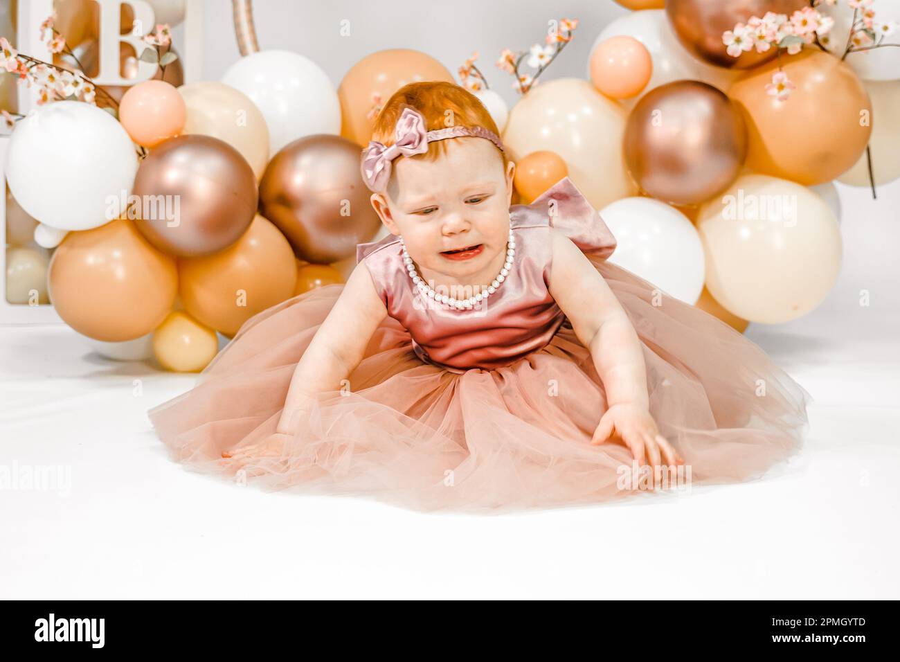 Little crying unhappy redhead baby girl celebrates first birthday anniversary. 1 year family party Professional photoshoot in photo studio. Cute adora Stock Photo