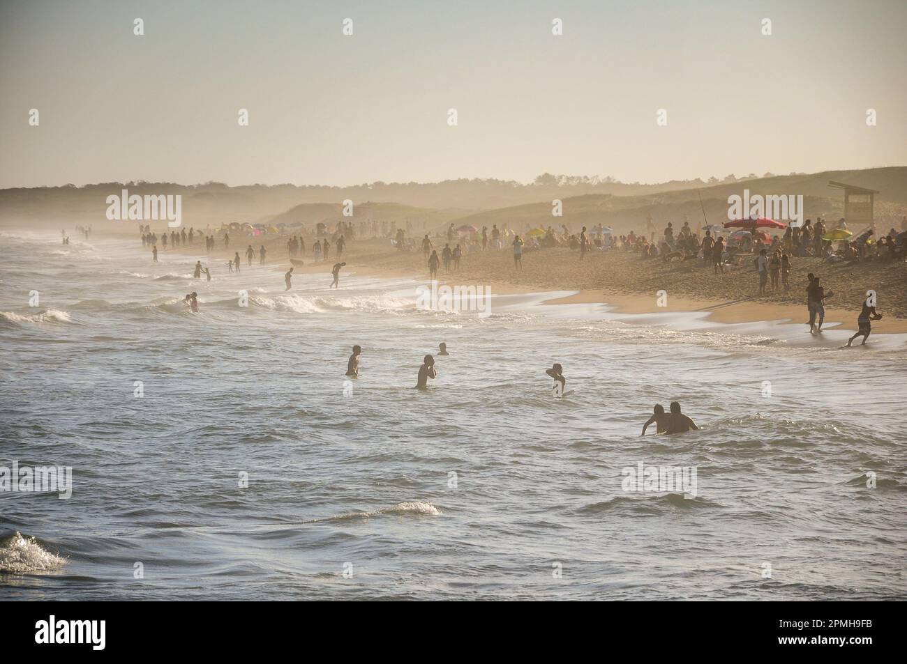 dozens of people bathing in one of the beaches of Punta del Diablo, during sunset Stock Photo