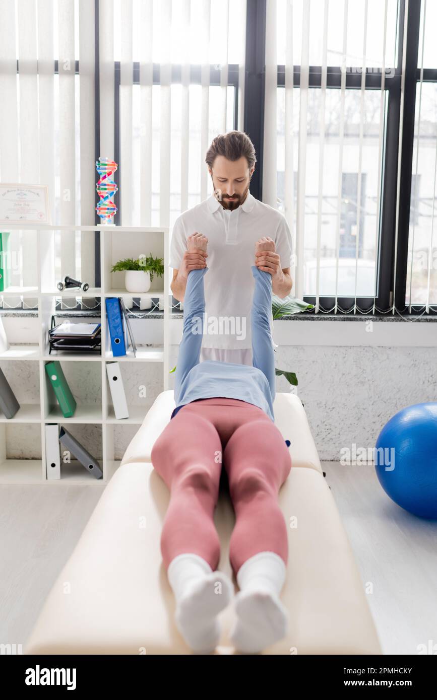 bearded manual therapist stretching arms of woman during recovery