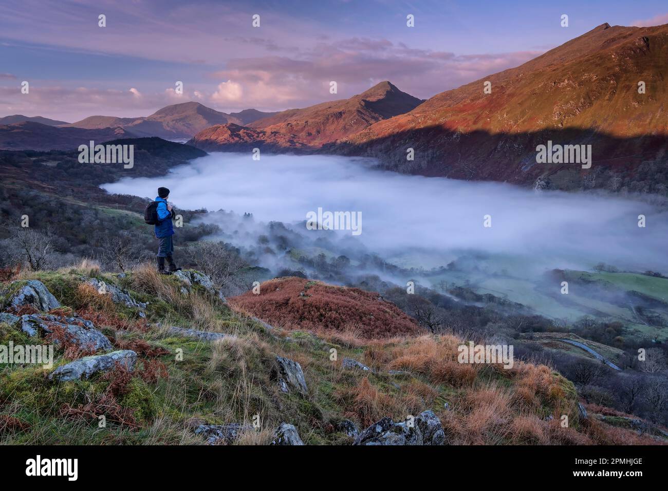 Walker looking out over the peak of Yr Aran and a fog filled Nant Gwynant Valley, Nant Gwynant, Eryri, Snowdonia National Park, North Wales, United Ki Stock Photo