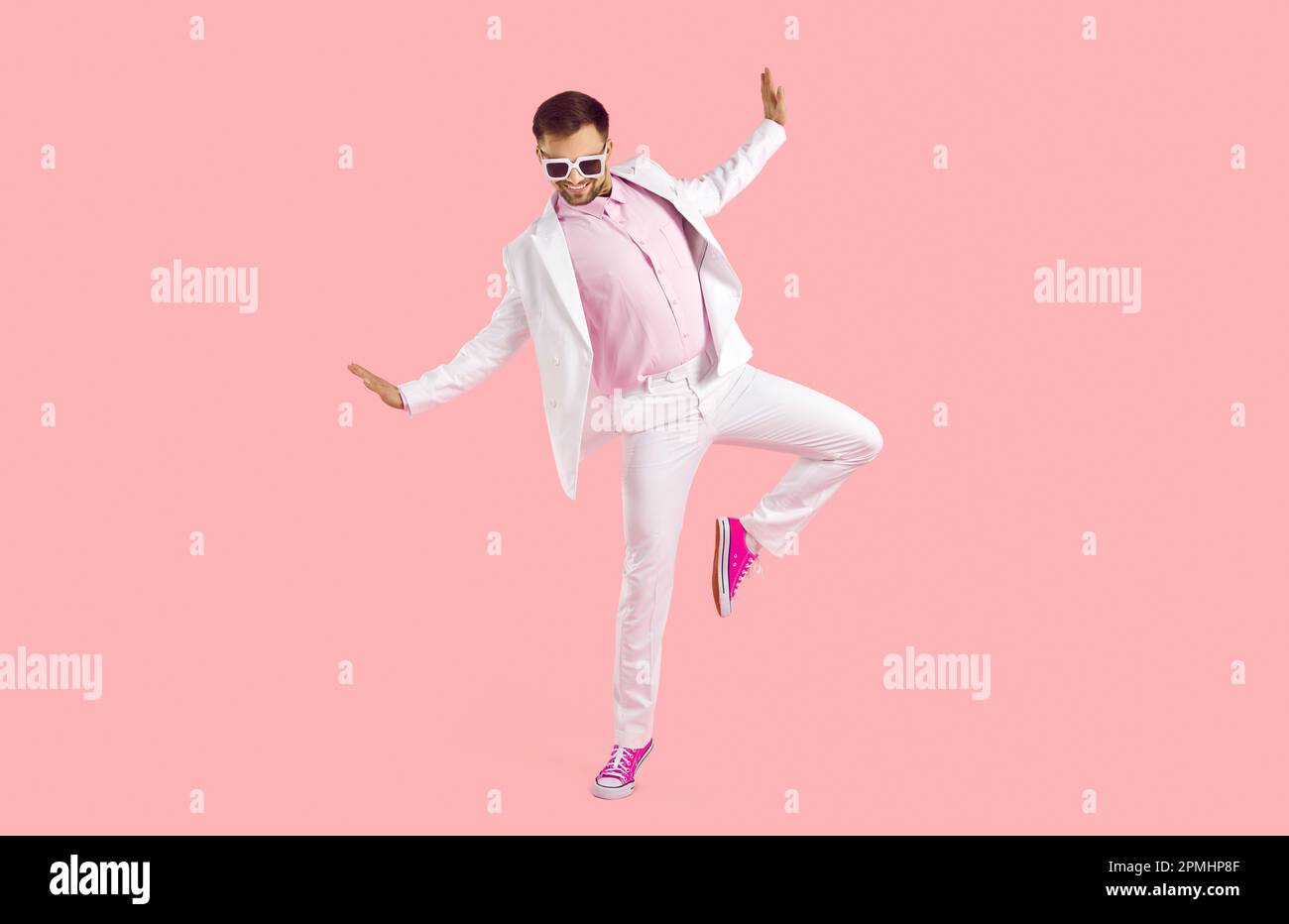 Funny young man in white suit, glasses and trainers dancing isolated on