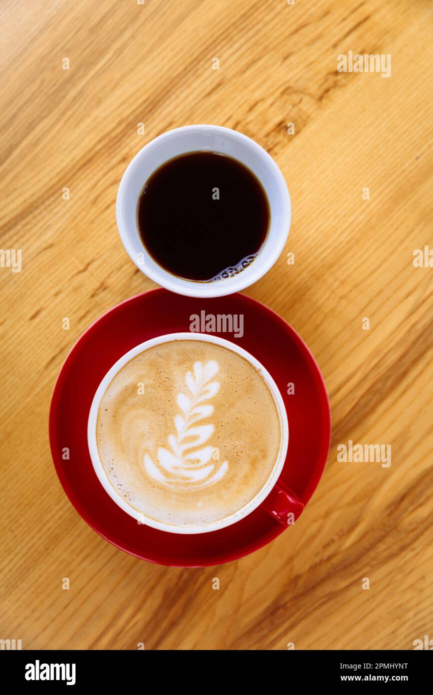 Aromatic coffee in a red cup with milk foam and latte art and freshly brewed coffee in a white cup on a light wooden table. The choice of coffee. Flat lay Stock Photo