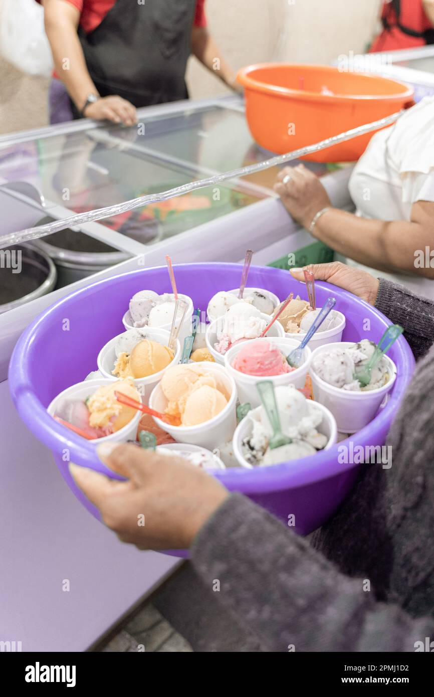 An adult Hispanic woman is holding a nest full of prepared ice creams