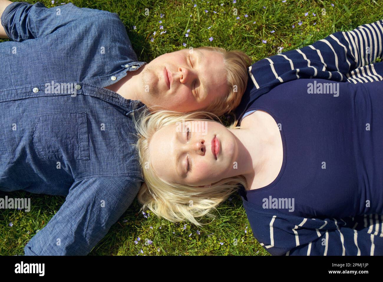 young couple laying on grass with eyes closed and their heads side by side enjoying the sun Stock Photo