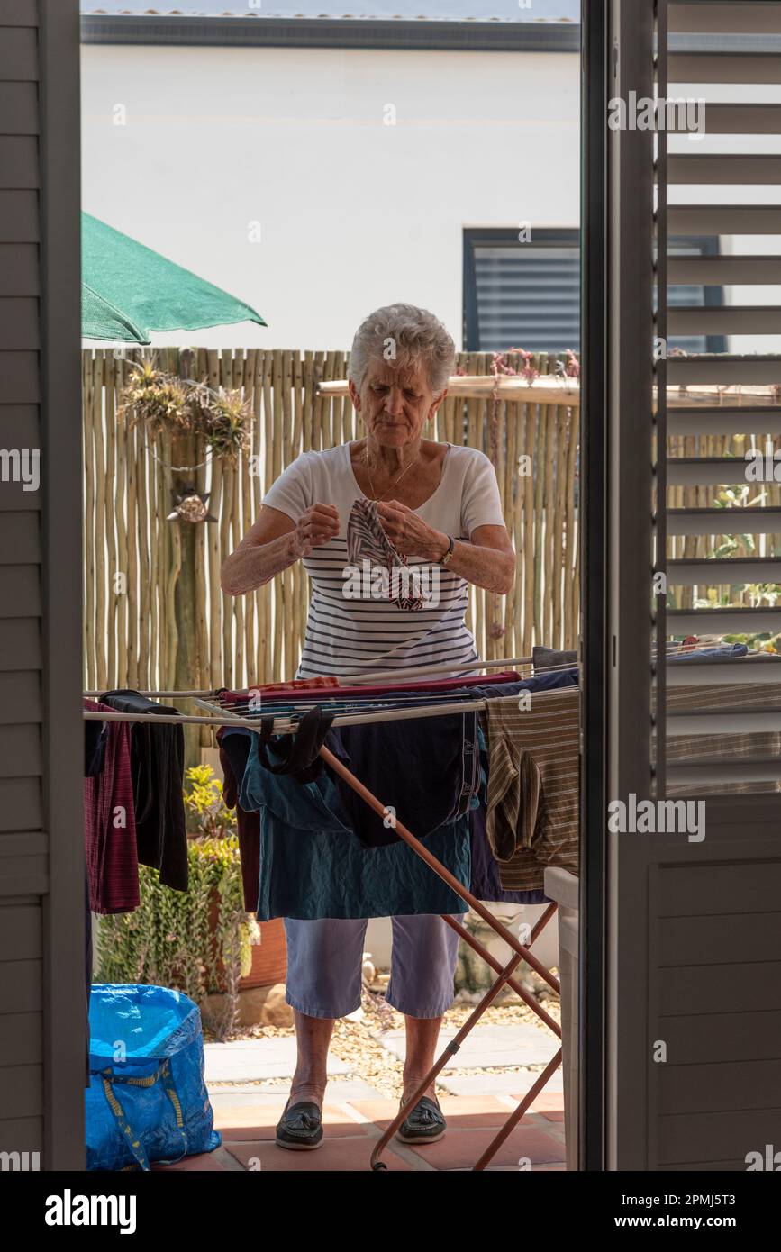 Langebaan, South Africa. 2023. White elderly woman sorting the washing and putting out to dry on a patio. Stock Photo