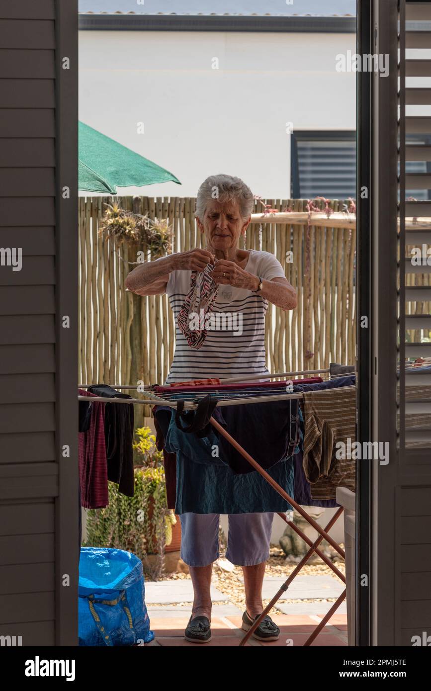 Langebaan, South Africa. 2023. White elderly woman sorting the washing and putting out to dry on a patio. Stock Photo