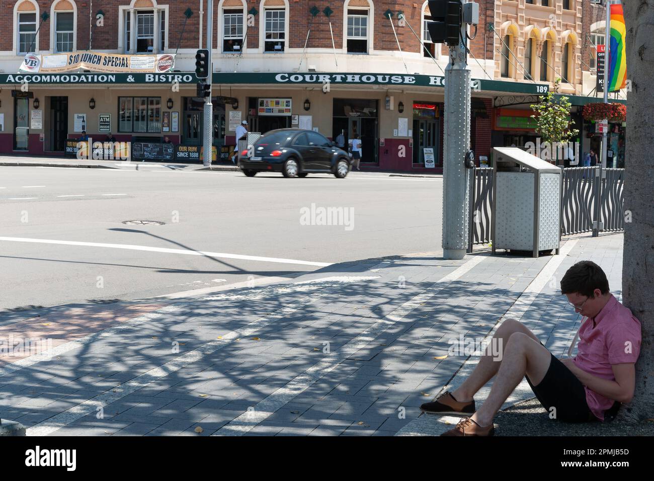 Sydney Australia - January 26 2011; person in pink shirt sits on ground under tree on side of Oxford Street across road from Courthouse Hotel. Stock Photo