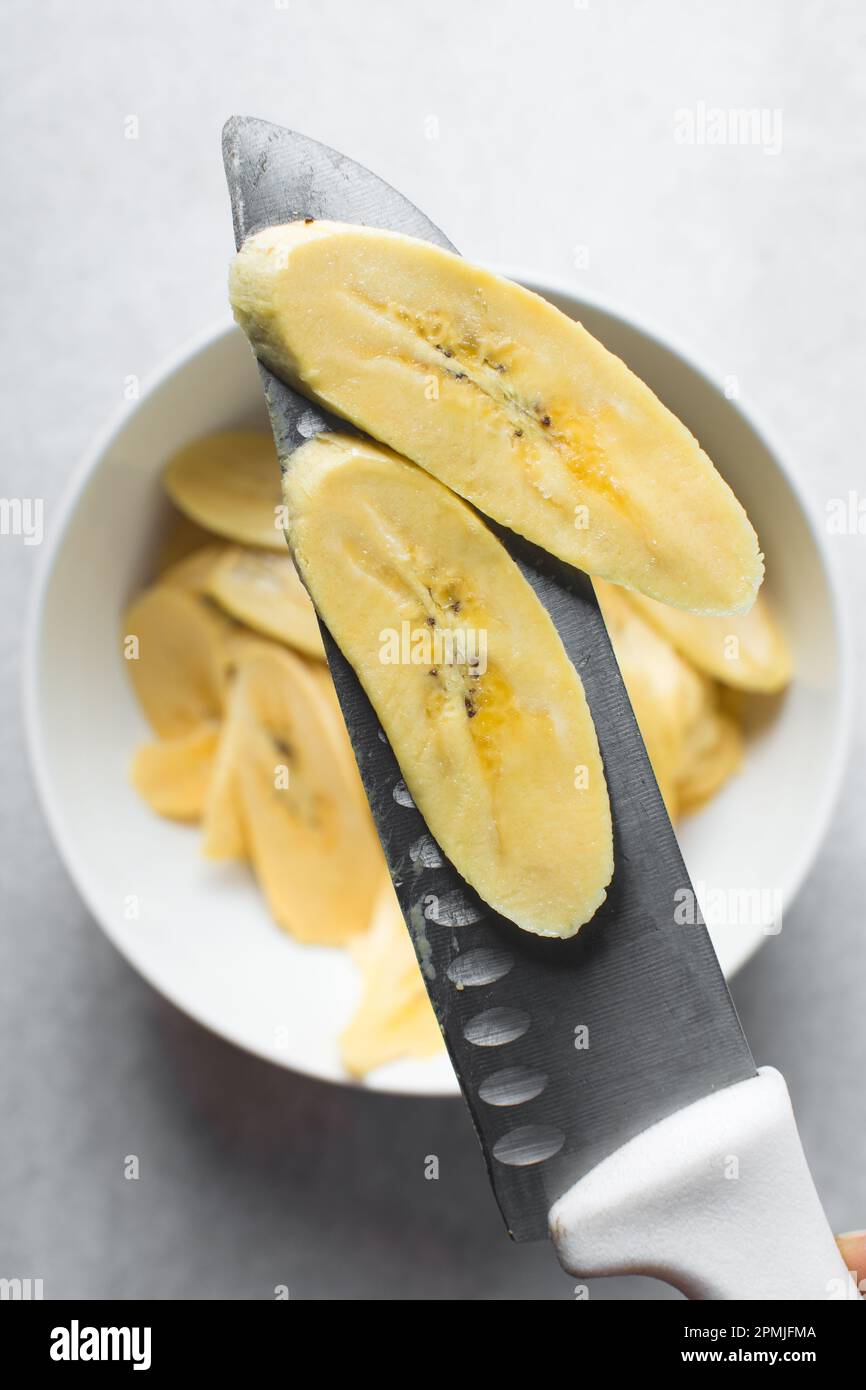 Hands slicing plantain, slicing yellow plantains for frying, process for making fried plantain Stock Photo