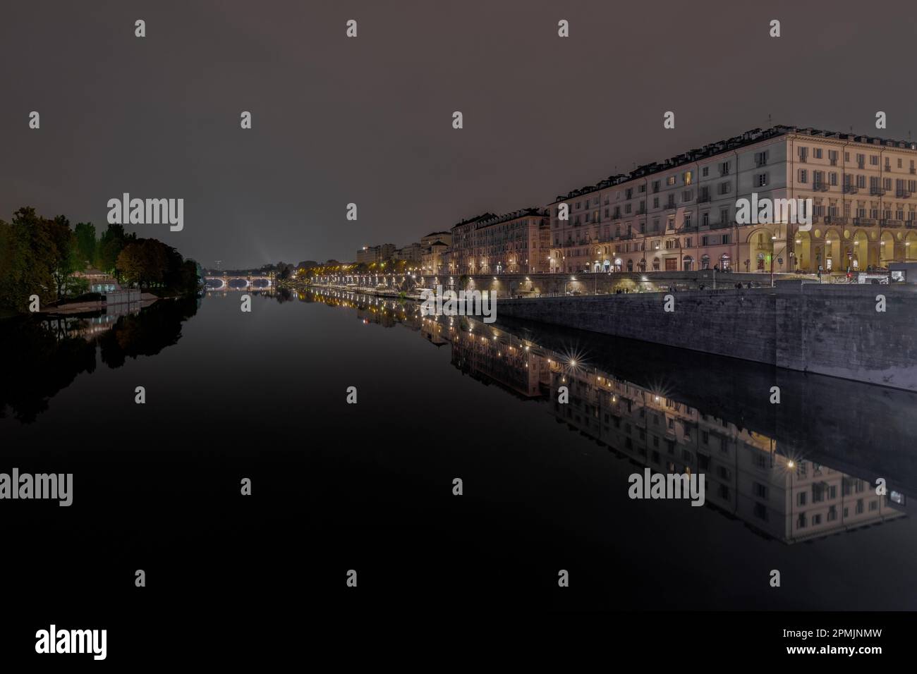 A scenic night view of a city canal illuminated by the streetlights in Murrazi, Turin, Italy Stock Photo