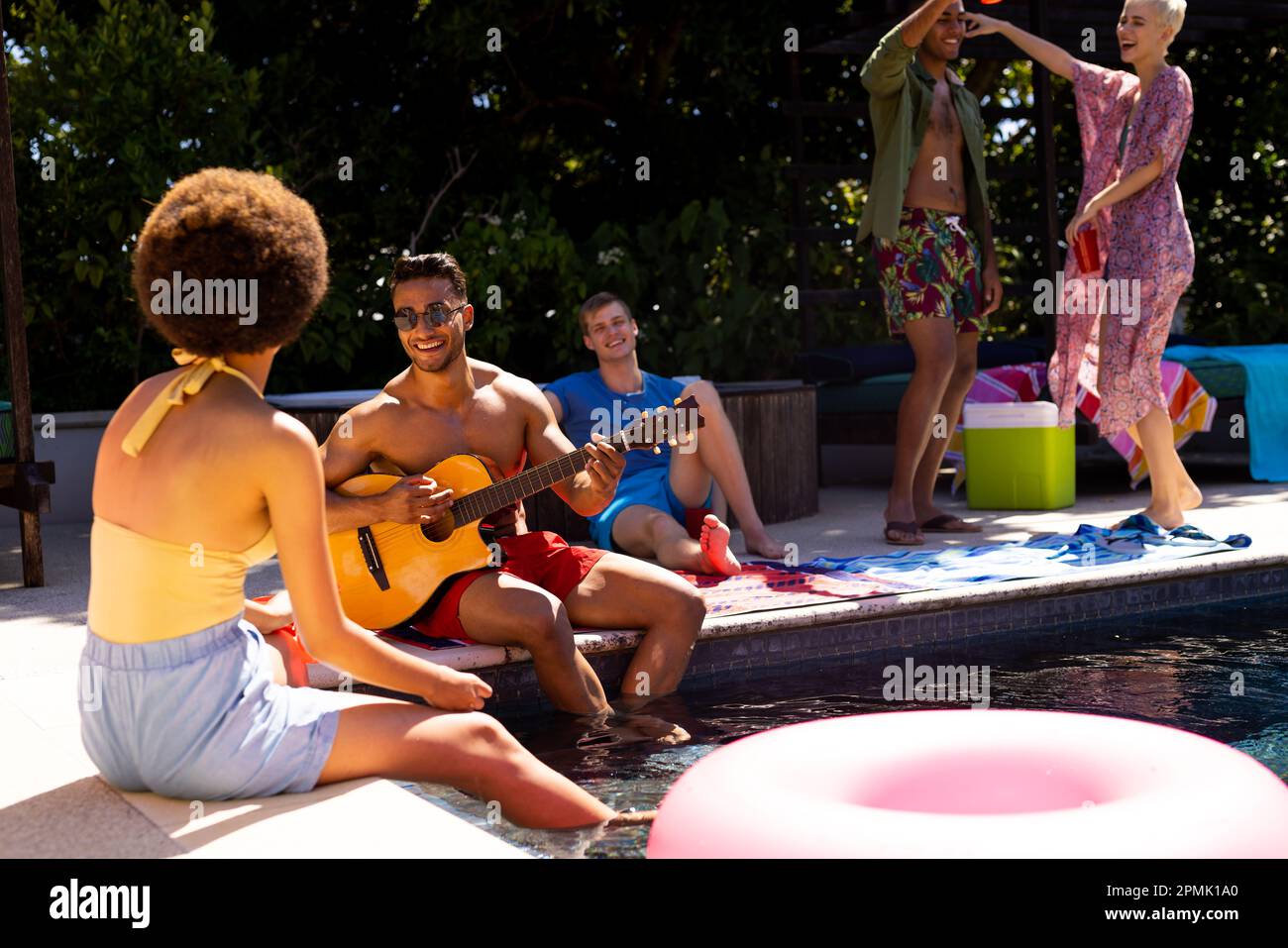 Happy diverse group of friends having pool party, playing guitar and ...