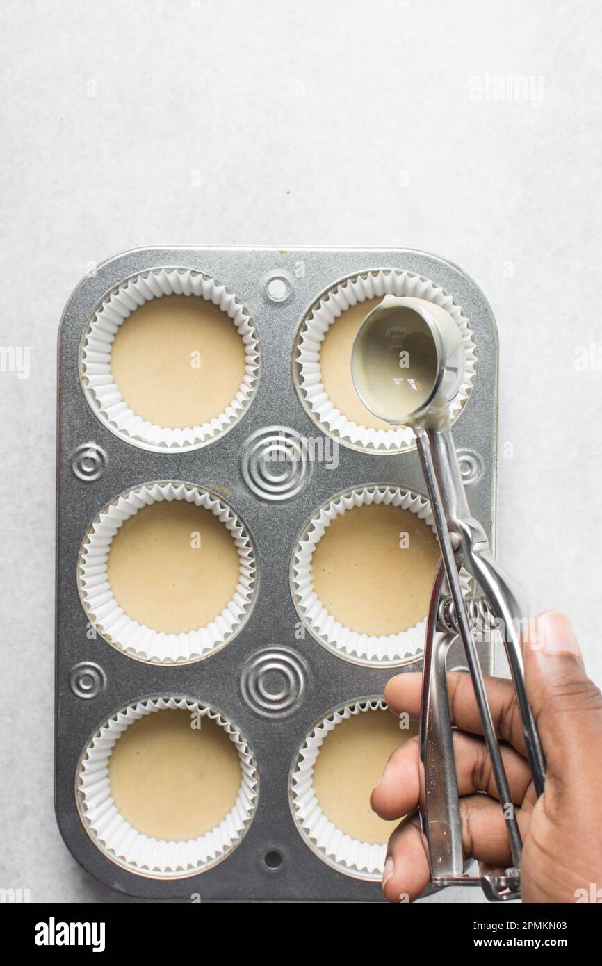 Hand scooping vanilla cake batter into a cupcake tin, An ice cream