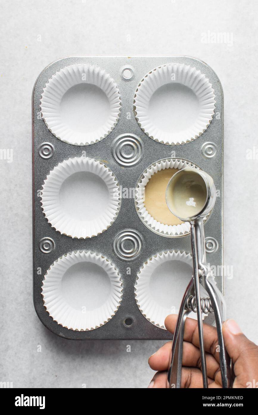 Hand scooping vanilla cake batter into a cupcake tin, An ice cream