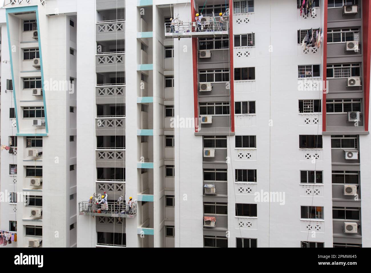 Wide view of 2 scaffold lifts hanging outside a block, the workers are busy painting the HDB building with a fresh coat of paint. Singapore. Stock Photo