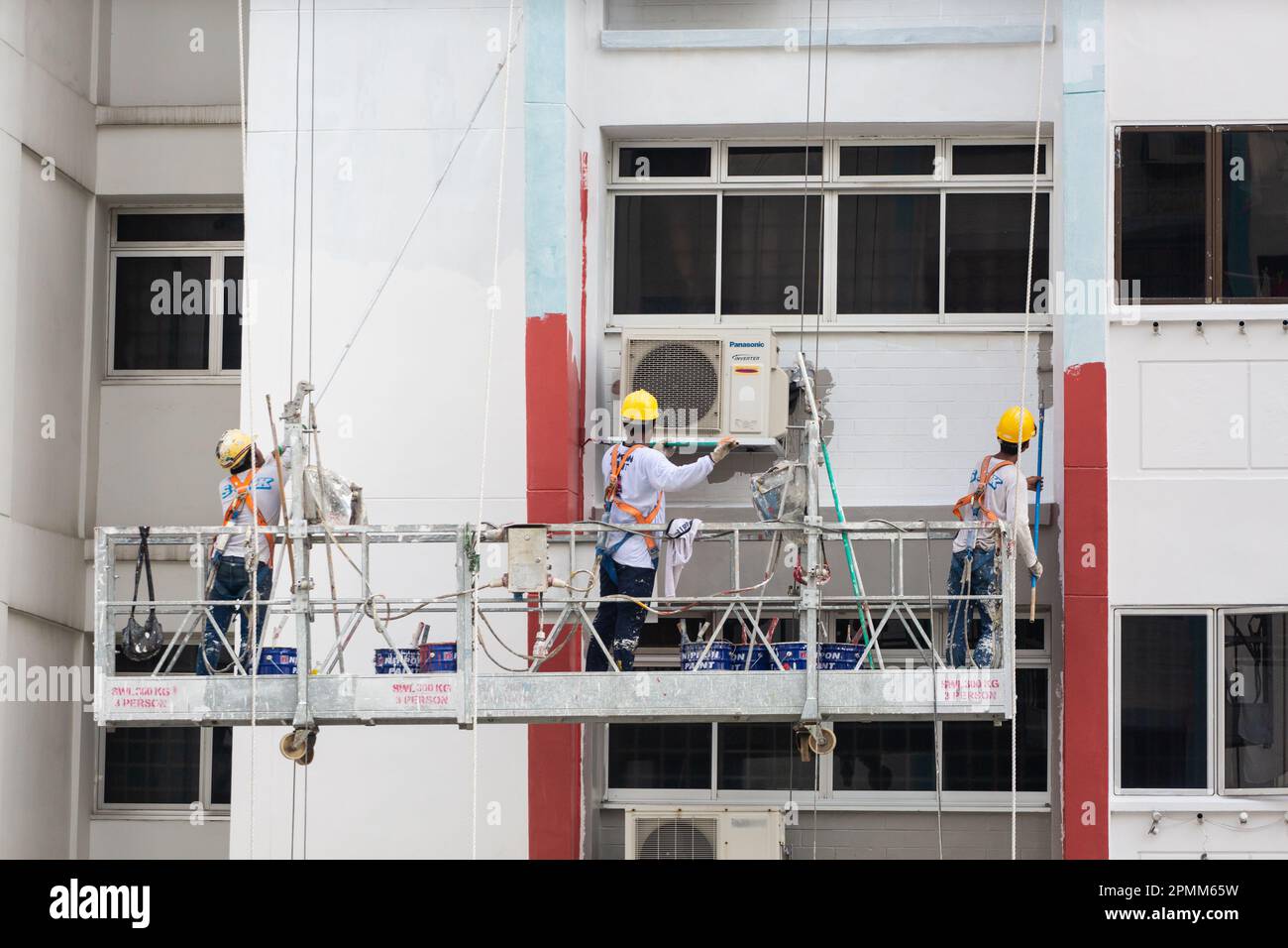 Close up of scaffolding lift with 3 painters are painting a fresh coat of paint on the housing exterior to give a fresh look. Singapore. Stock Photo