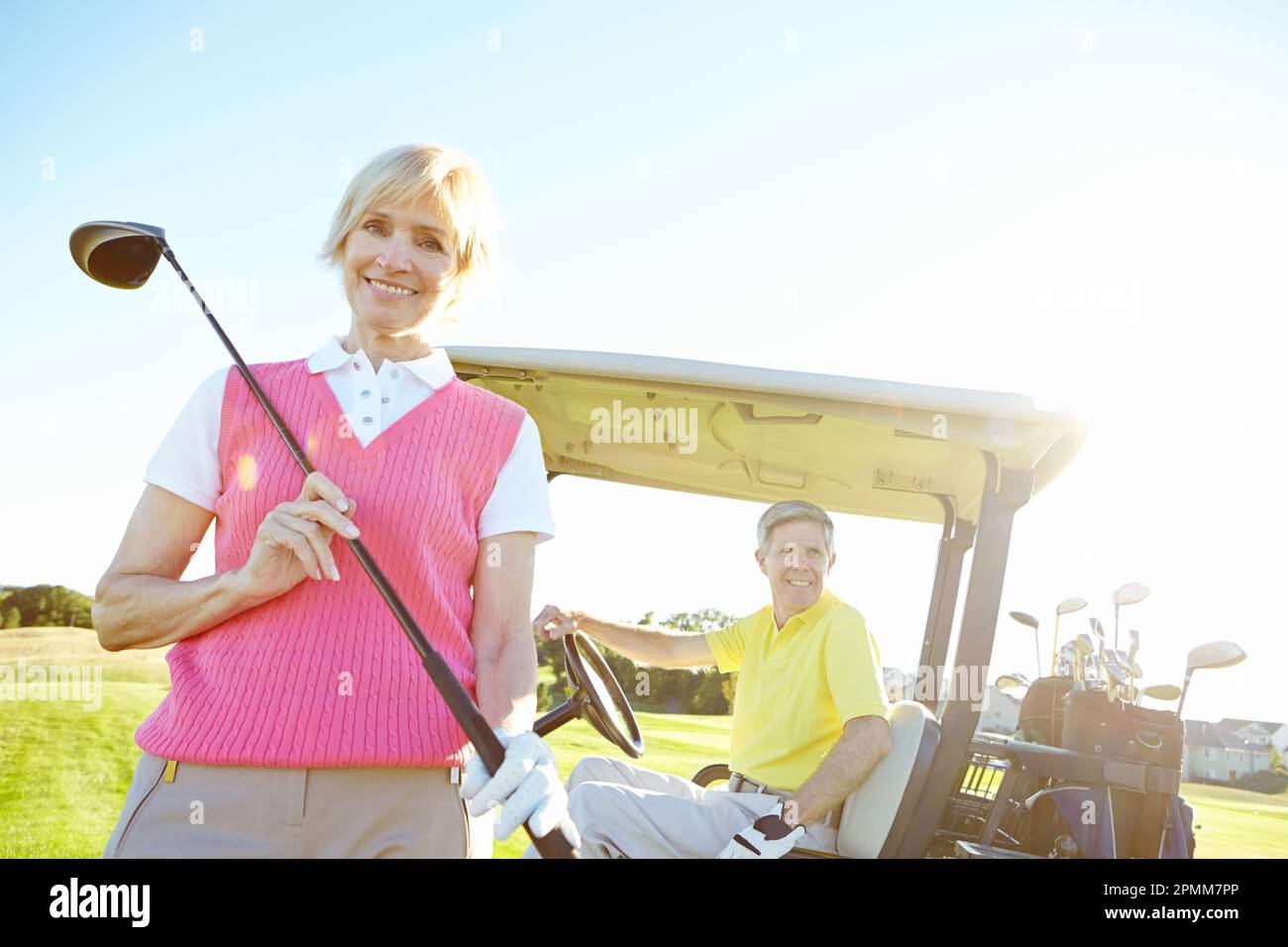 Spot of golf. Low angle shot of an attractive older female golfer standing in front of a golf cart with her golfing buddy behind the wheel. Stock Photo