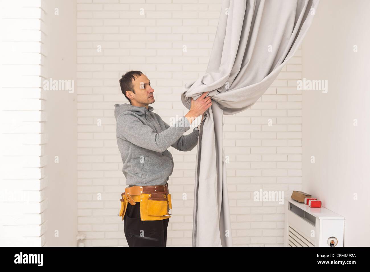 worker installing window curtain rod on the wall. Stock Photo