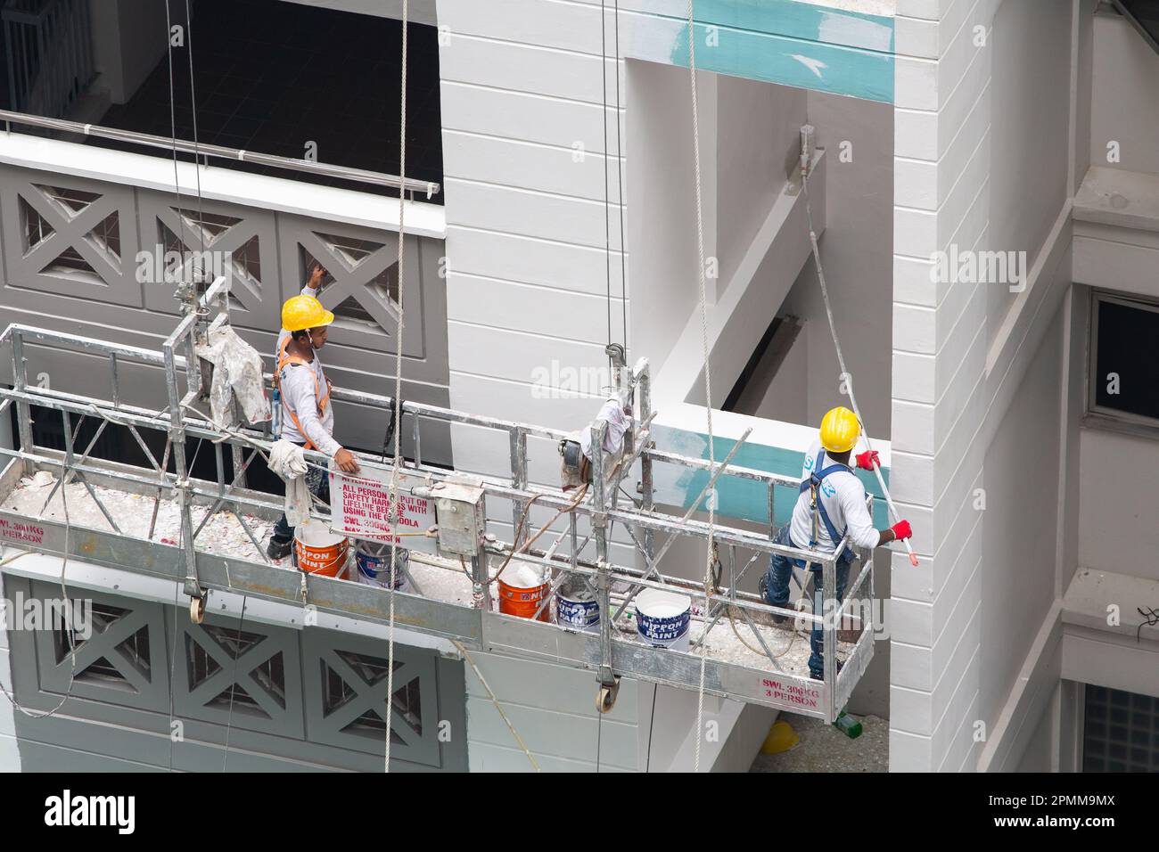 Two painters on scaffold lift painting fresh of white paint on the