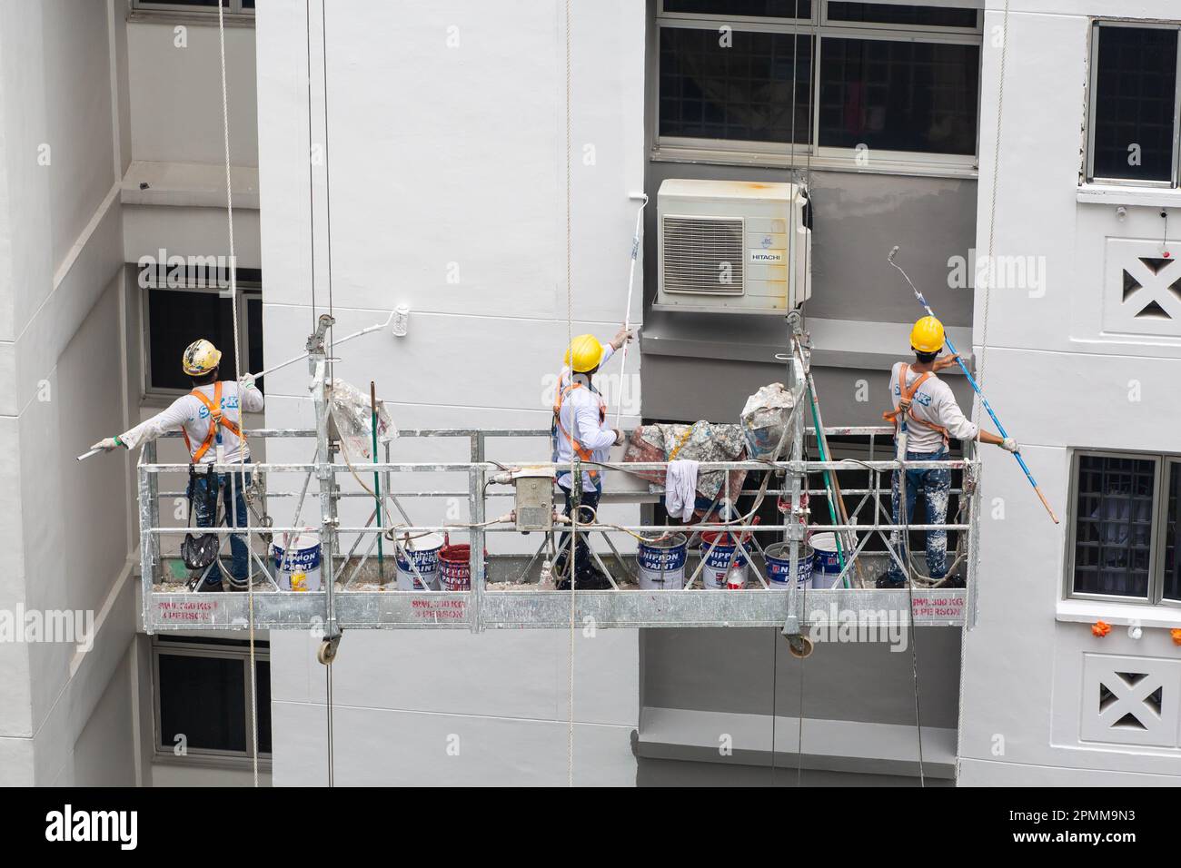 Three workers with safety helmet on scaffold lift painting fresh paint